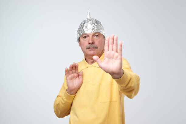 Caucasian mature man in a tin foil hat displeased closing his face with hands. Caucasian mature man in a tin foil hat displeased hiding from outdoor life. Afraid of radiation or aliens. Stop sign conspiracy stock pictures, royalty-free photos & images