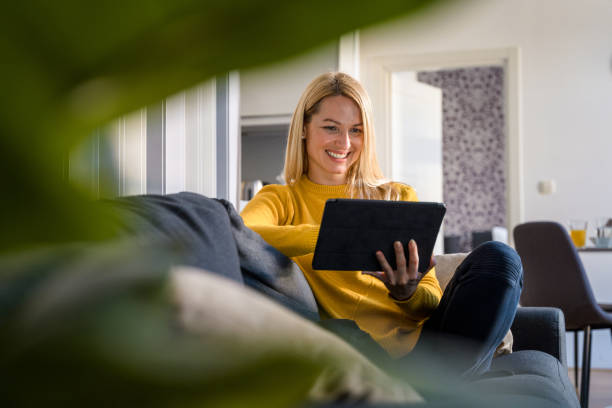 Caucasian Mid Adult Woman Using Digital Tablet and Having Video Call on Sofa at Home stock photo