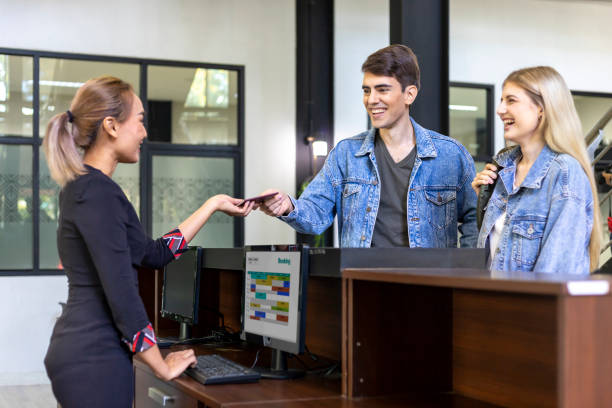 Caucasian tourist couple is handing passport to the reception at hotel lobby counter for check in to the room for international travel and vacation concept stock photo