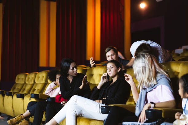 Caucasian using mobile phone and loud talking in movie theater. stock photo