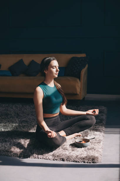 Caucasian woman practicing yoga at home sitting on carpet with closed eyes breathing fresh air. No stress free. Lotus position. Meditation practice. stock photo