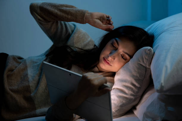 Caucasian women are using the tablet computer on the bed before she sleeping at night, Mobile addict concept, Blue light harmful to the eyes. stock photo