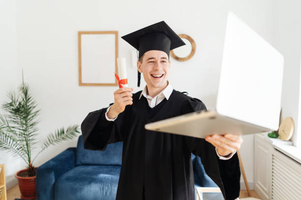 Caucasian young man feeling very excited to receive his bachelors degree Education, graduation and people concept - happy male student with diploma and laptop at home showing his emotions bachelor’s degrees online stock pictures, royalty-free photos & images