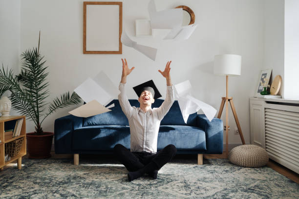 Caucasian young man feeling very excited to receive his bachelors degree Education, graduation and people concept - top view of happy male student throwing a bunch of sheets at home showing his emotions bachelor’s degrees online stock pictures, royalty-free photos & images