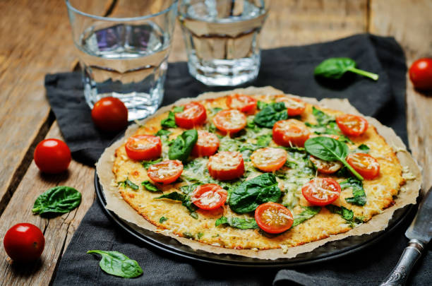 Cauliflower pizza crust with tomato and spinach Cauliflower pizza crust with tomato and spinach. toning. selective focus pastry dough stock pictures, royalty-free photos & images