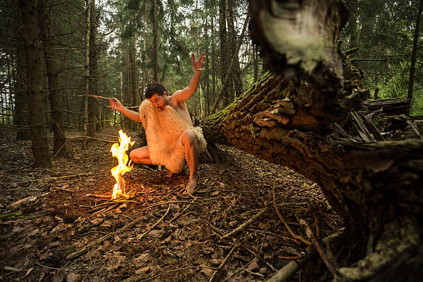 caveman in animal skin kindles a fire in the forest - fire caveman imagens e fotografias de stock
