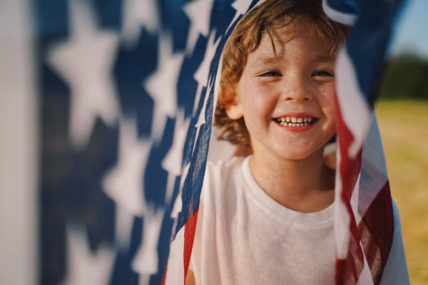 сша празднуют 4 июля. счастливый маленький мальчик патриот работает в поле с американским флагом. - july 4 стоковые фото и изображения