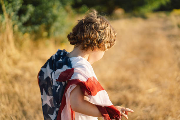 сша празднуют 4 июля. счастливый маленький мальчик патриот работает в поле с американским флагом. - july 4 стоковые фото и изображения
