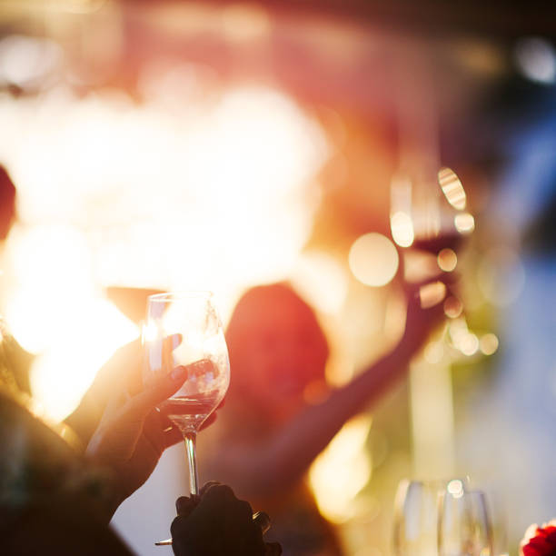 Celebratory wine toast between adult friends at social event party at sunset square shot stock photo