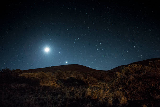 Celestial Bodies Formations of planets and stars rise over a dark mountain ridge. mauna kea stock pictures, royalty-free photos & images