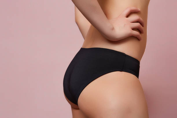 cellulite of a young girl in a black swimsuit . on a pink isolated background stock photo