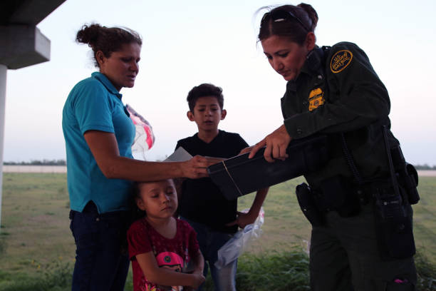 Central American Refugees, South Texas August 16, 2017 - McAllen, Texas, USA - A Border Patrol agent takes a young Honduran woman and her two children who had just crossed the Rio Grande River seeking asylum into custody.  A steady stream of Central Americans, ranging from single children to entire families fleeing gang violence, continue to make the dangerous journey across Mexico to the U.S. border patrol stock pictures, royalty-free photos & images