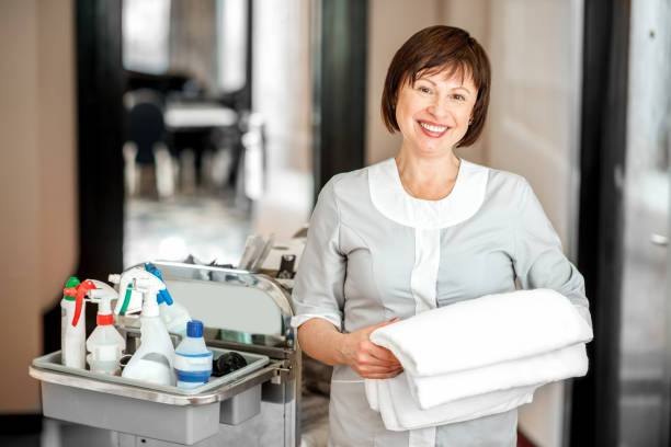 Chambermaid in the hotel corridor Portrait of a senior woman chambermaid standing with towel and maid cart full of cleaning stuff in the hotel corridor maid stock pictures, royalty-free photos & images