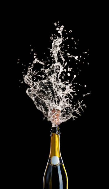 champagne bottle with cork flying with splashing liquid on black. stock photo