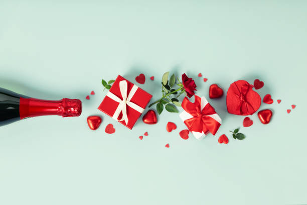Champagne bottle with gift boxes, roses, chocolate and red hearts on blue background, top view, flat lay, banner. stock photo
