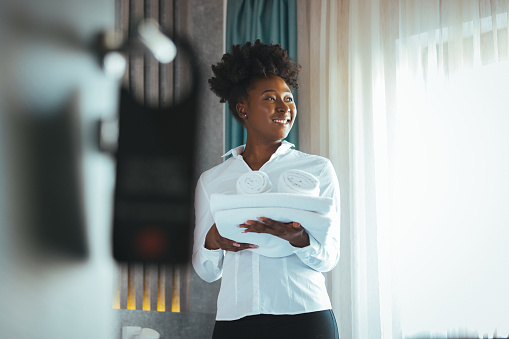 Close up of a young hotel maid holding clean folded towels. Chambermaid holding clean towels in hotel room. Cleaning the hotel room. Copy space. The concept of the hotel business.