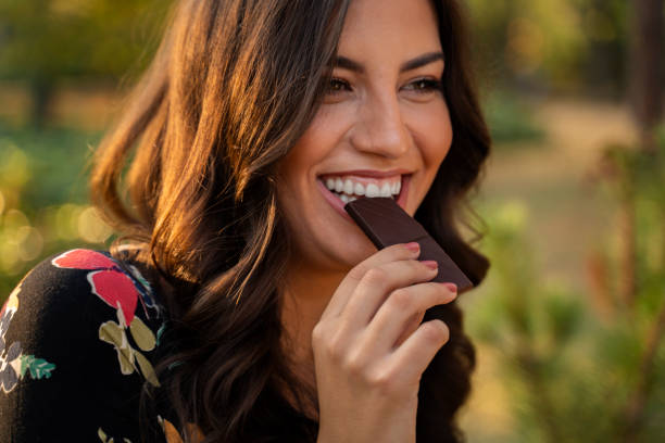 charismatische vrolijke jonge vrouw die chocolade eet en glimlacht - chocolade stockfoto's en -beelden