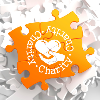 Charity Word Written Arround Icon of Heart in the Hand, Located on Orange Puzzle. Social Concept.