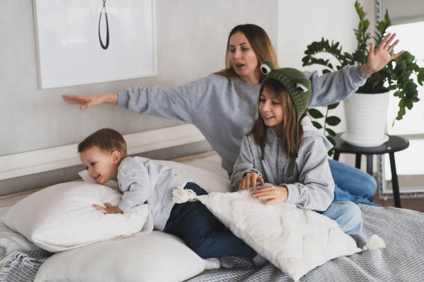 charming mother and her children, daughter and little son have fun at home on the bed stock photo
