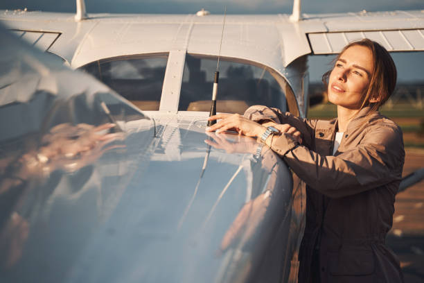 Charming young woman standing near plane at airdrome stock photo