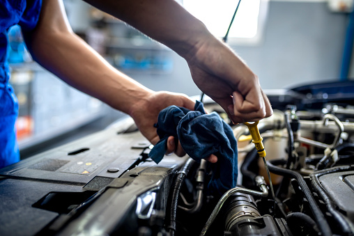 Photo of Unrecognizable male mechanic measuring the oil level of an engine at an auto shop. Mechanic checking the oil level in a car service garage. Repairing engine at a service station. Car repair.\