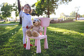 Cute and gorgeous child playing in the park as a doctor, taking care of her teddy bear.