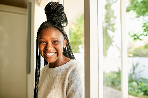 Portrait of a cheerful african teenage girl with braided hairstyle walking in the house from the entrance door