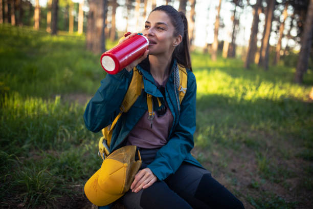A cheerful and tired mountaineer rests in the woods and drinks water. stock photo