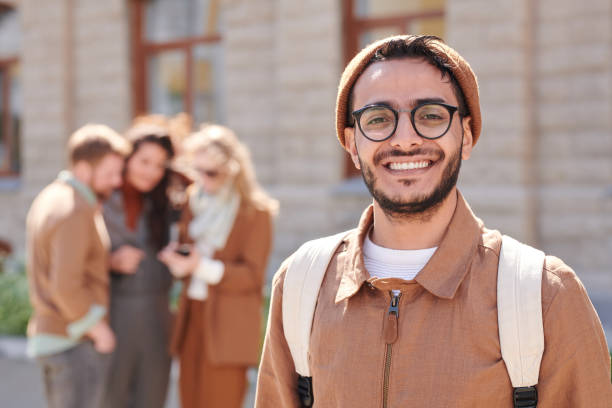 Cheerful Arabian man in eyeglasses outdoors Portrait of cheerful young Arabian man in eyeglasses and beanie hat travelling with friends old arab man stock pictures, royalty-free photos & images