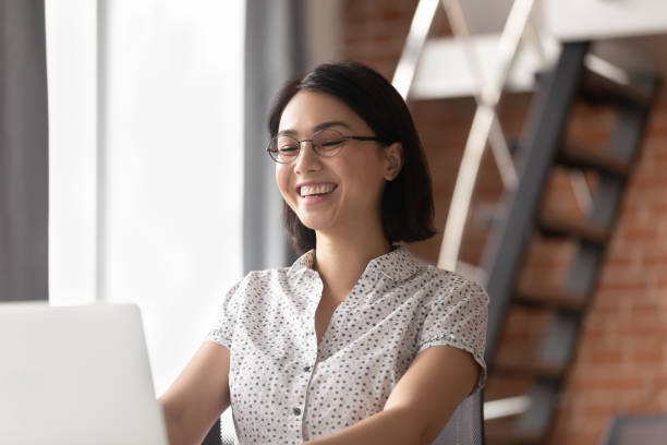 Cheerful asian business woman laughing looking at laptop computer...