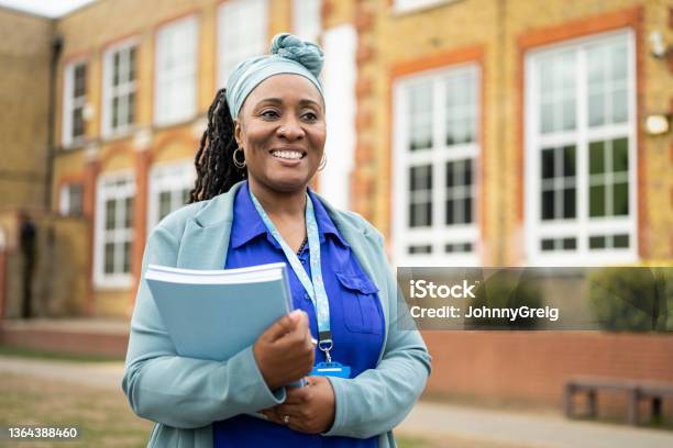 Cheerful Black teacher standing outside education building
