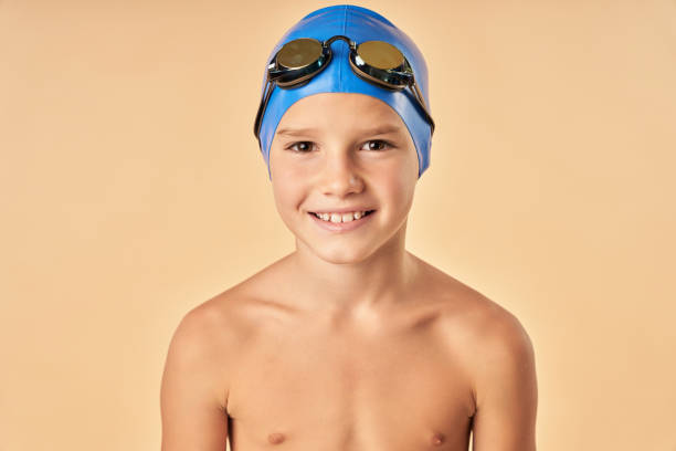 Cheerful boy swimmer standing against light orange background stock photo