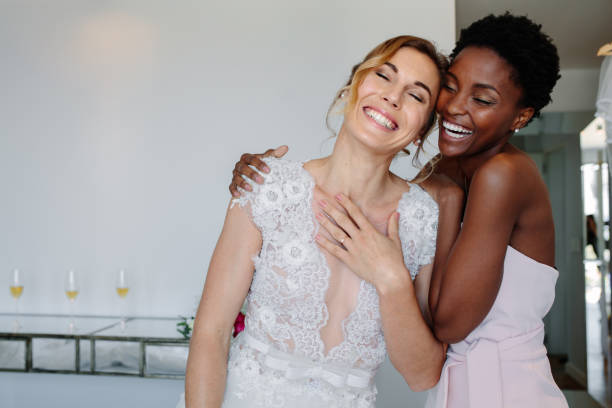 Cheerful bride and bridesmaid on the wedding day Gorgeous bride in wedding gown having fun with bridesmaid in hotel room. Cheerful bride and bridesmaid on the wedding day. bride stock pictures, royalty-free photos & images