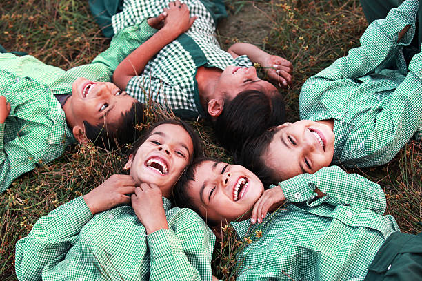 cheerful children lying dawn on grass Group of cheerful children wearing school uniform lying down on grass & laughing elevated view. haryana stock pictures, royalty-free photos & images