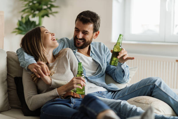 Cheerful couple having fun while drinking beer at home Young happy couple communicating while sitting on the sofa and drinking beer alcohol drink stock pictures, royalty-free photos & images