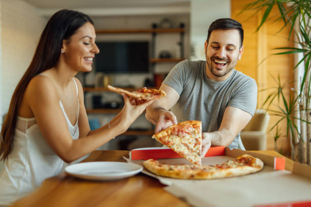 Cheerful couple in pajamas eating pizza at home, portrait. stock photo