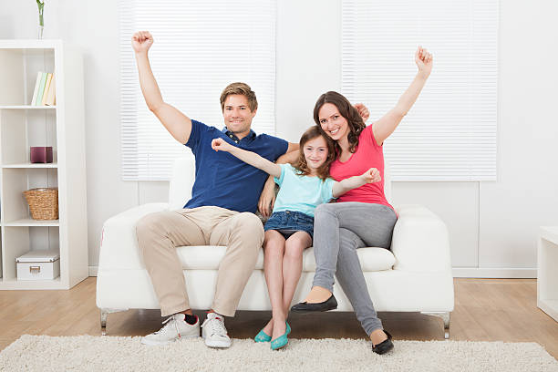 Full length portrait of cheerful family with arms raised sitting on...