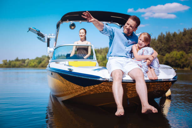 Cheerful father telling daughter stories while sailing boat Interesting stories. Cheerful young father pointing at riverbanks and telling his little daughter stories while they sitting on the bow of the boat motorboat stock pictures, royalty-free photos & images