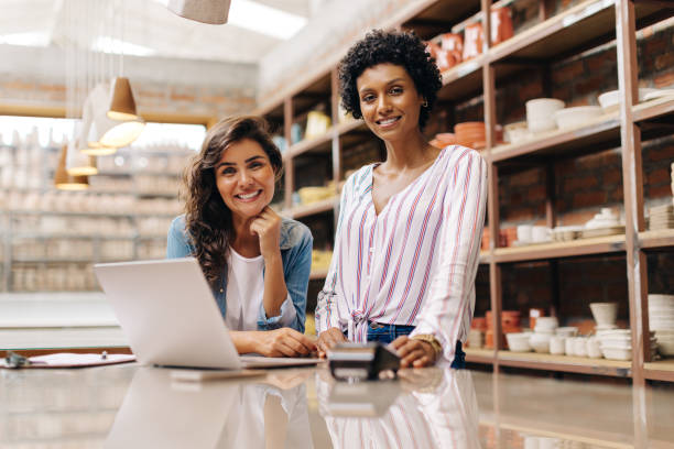 Cheerful female entrepreneurs smiling at the camera in their ceramic shop stock photo