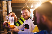 Cheerful football fans are saluting to each other with beer pints while laughing and having a discussion about a sport.