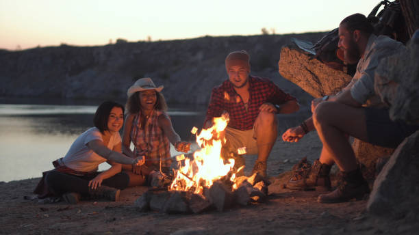 vrolijke vrienden ontspannen rond het kampvuur - beach game group stockfoto's en -beelden
