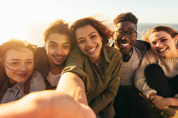 Cheerful friends taking selfie on a holiday Cheerful friends taking selfie on a holiday. Group of men and women sitting outdoors on a summer day making self portrait. hiking photos stock pictures, royalty-free photos & images