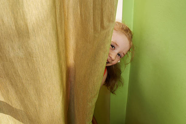 cheerful girl looks out from behind  curtains stock photo