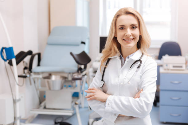 Cheerful gynecologist waiting for the next patient in the cabinet Full of joyful emotions at work. Positive delighted qualified gynecologist standing in the gynecology cabinet while expressing positivity and enjoying working responsibilities gynecologist photos stock pictures, royalty-free photos & images