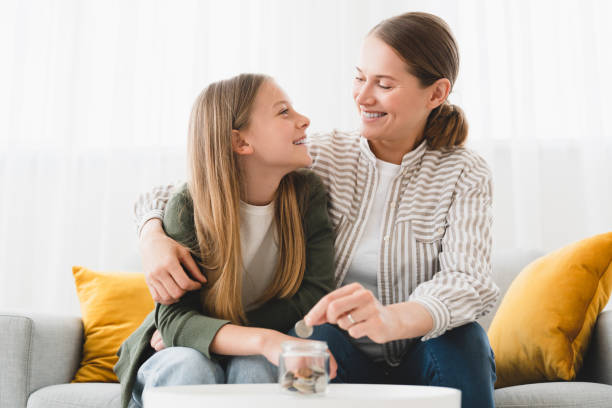 Cheerful happy young family of mother mom and daughter saving money, putting coins in bank, planning future, paying bills, loan. Nest egg concept. stock photo