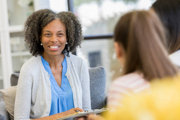 Cheerful high school guidance counselor talking with students Encouraging mature high school guidance counselor smiles as she discusses education options with female high school students. school counselor stock pictures, royalty-free photos & images