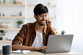 istock Cheerful indian guy businessman with laptop having phone conversation 1354244046