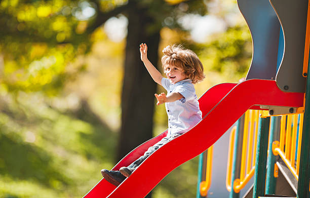 Cheerful little boy having fun while sliding outdoors. Happy little boy sliding outdoors with his arms raised. sliding stock pictures, royalty-free photos & images