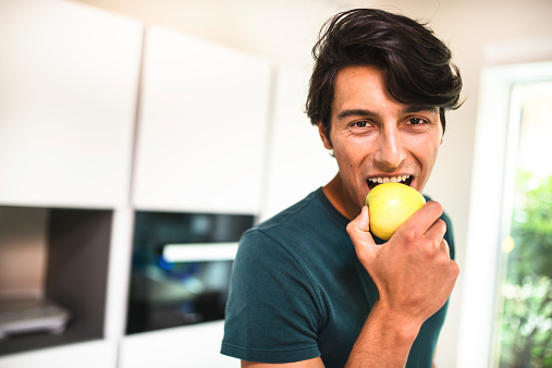 cheerful man eating an apple on kitchen