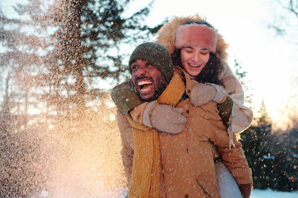 Cheerful multiracial couple in winterwear laughing while girl embracing her boyfriend stock photo